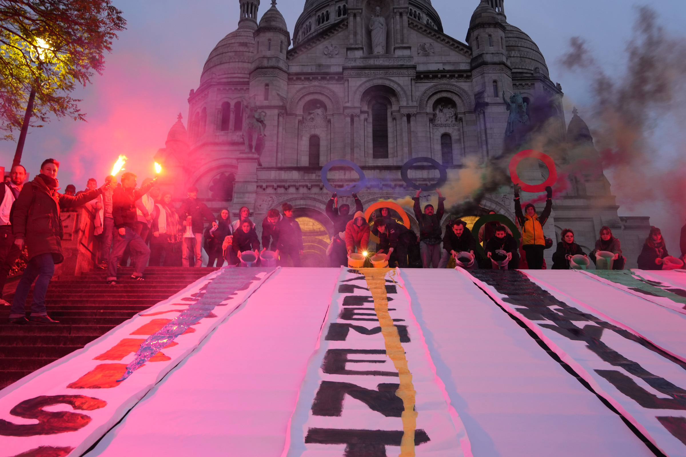 People protesting at Sacré-Cœur church in Paris, holding rings, flares, and pouring paint.