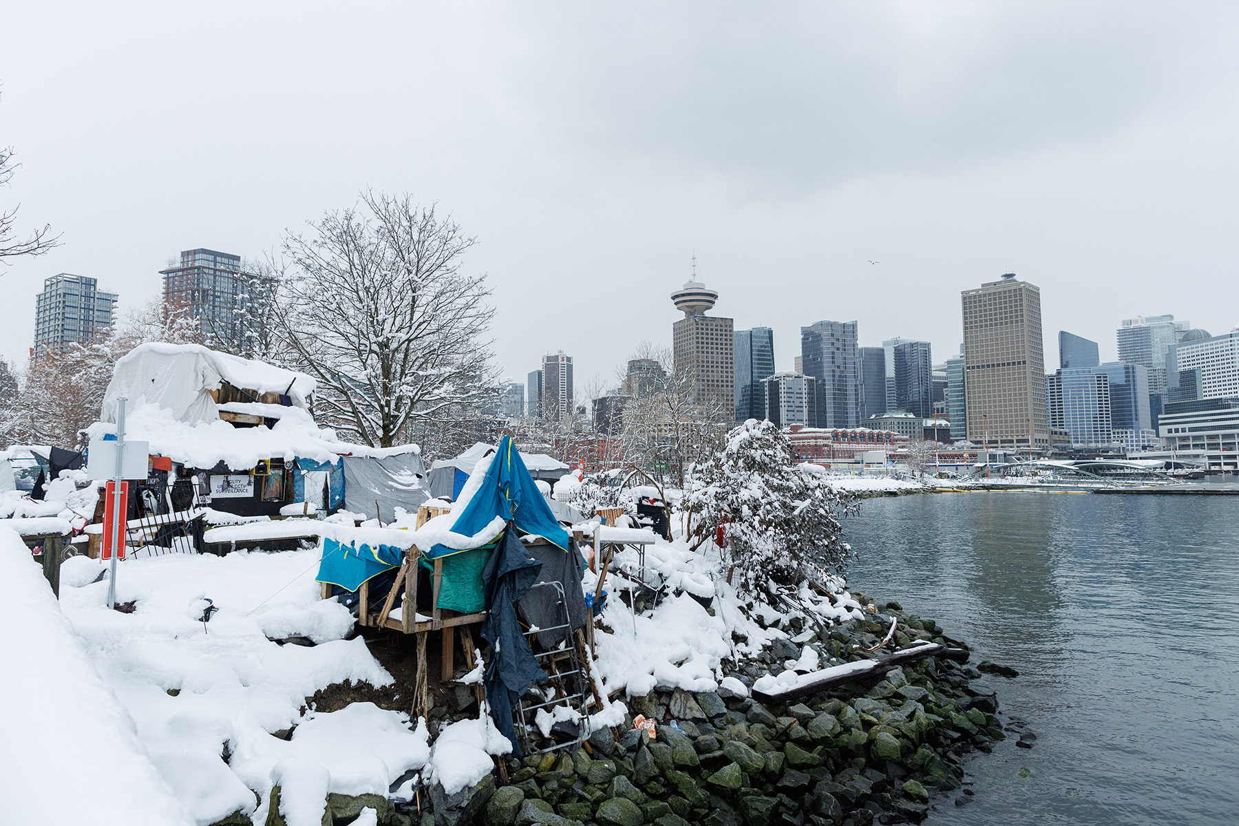 An encampment along the water's edge with the downtown Vancouver skyline in the background.