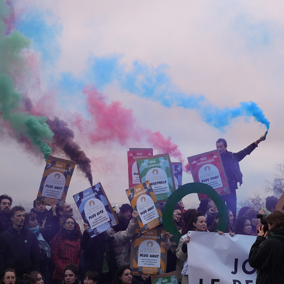 People protesting the Olympics in Paris with multi-coloured smoke and signs.