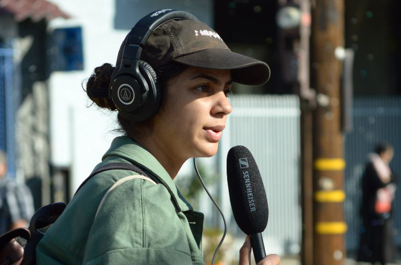 A woman in a green jacket and black hat holding audio recording equipment.